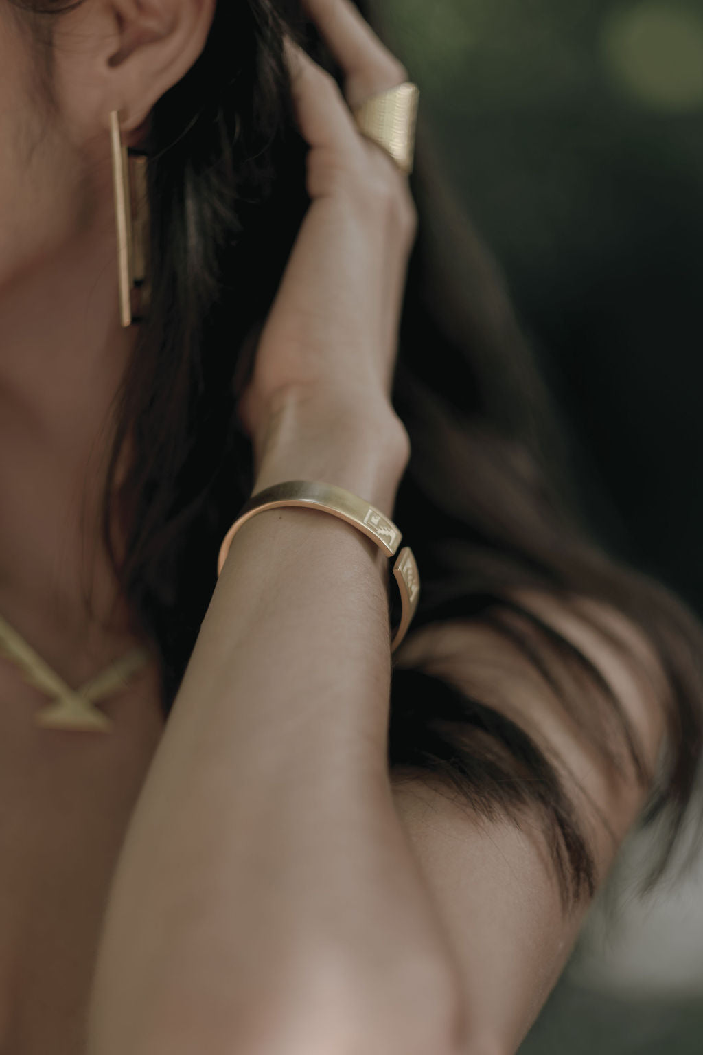 Close-up of a person wearing gold jewelry including earrings and a bracelet.