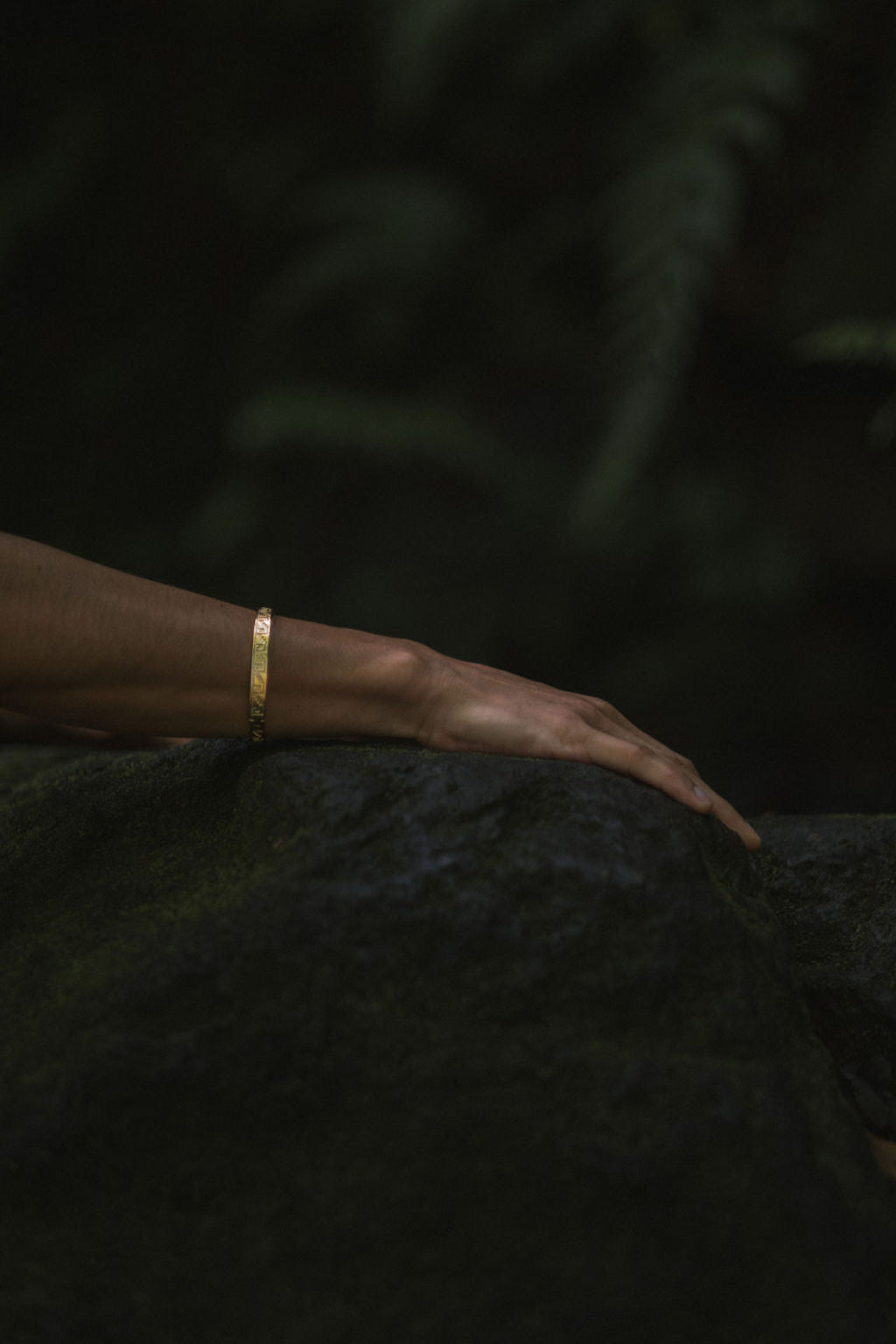 Gold bracelet on a person's wrist against a dark background